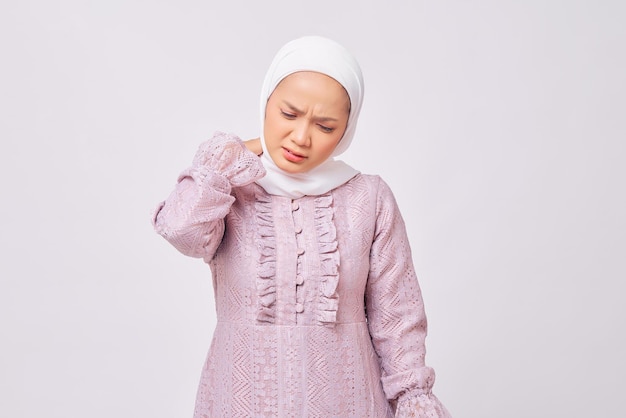 Retrato de uma bela jovem muçulmana asiática usando hijab e vestido roxo tocando seu pescoço sentindo-se cansada após longas horas de trabalho isoladas no fundo branco do estúdio