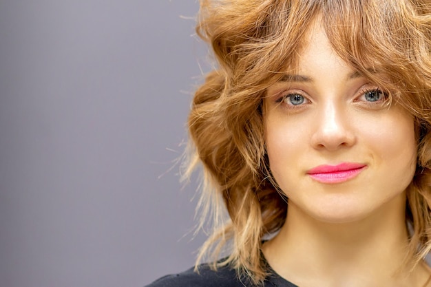 Retrato de uma bela jovem ruiva caucasiana com penteado ondulado curto sorrindo e olhando para a câmera no fundo cinza escuro com espaço de cópia