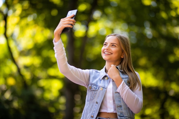 Retrato de uma bela jovem selfie no parque com um smartphone