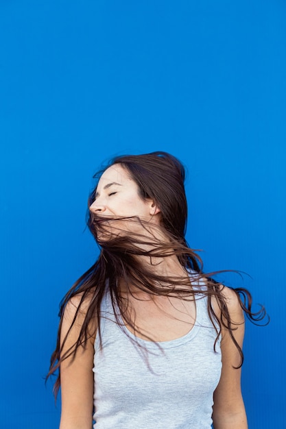 Foto retrato de uma bela jovem sorrindo e brincando com os cabelos e o vento com um fundo azul