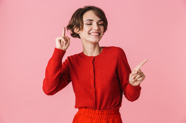 Retrato de uma bela jovem vestindo roupas vermelhas em pé isolado sobre um fundo rosa, dançando