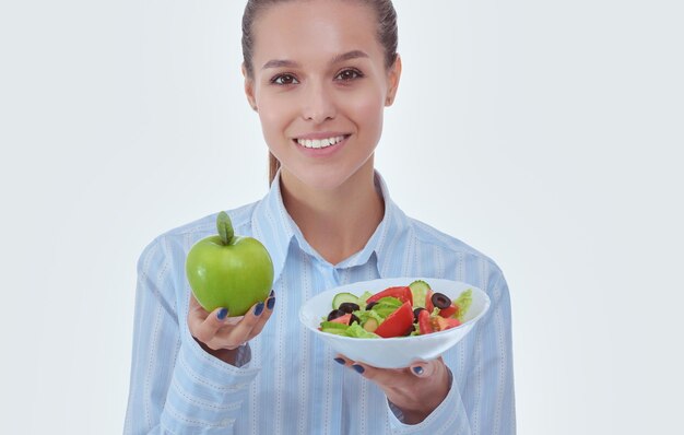 Retrato de uma bela médica segurando um prato com legumes frescos e maçã verde. Mulher médica