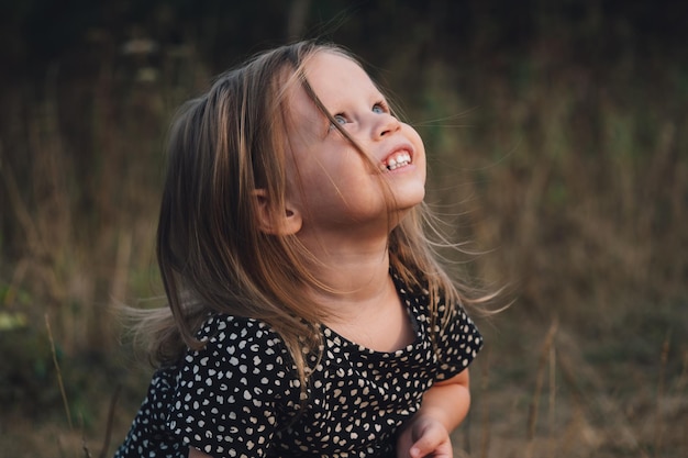 Retrato de uma bela menina loira europeia com olhos azuis na natureza uma criança pequena sonhadora e admirada olha para o céu de perto emoções sinceras das crianças