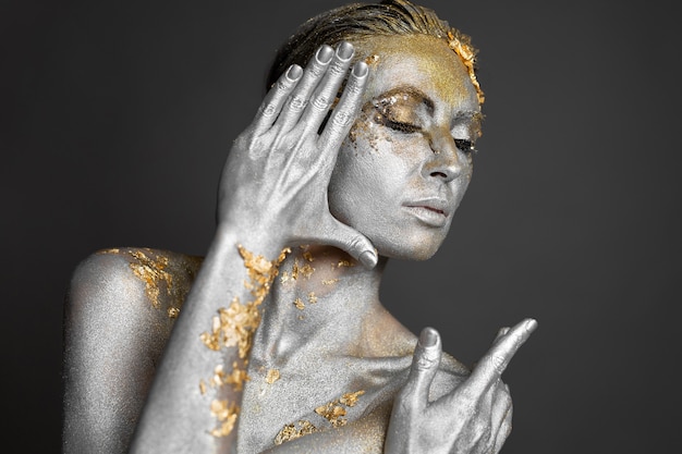 Retrato de uma bela modelo feminino com tinta dourada e prata na pele e no cabelo no estúdio.