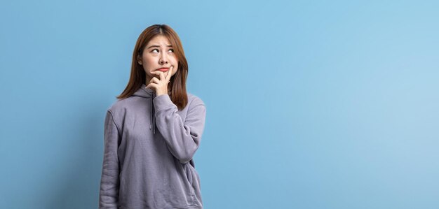 Retrato de uma bela mulher asiática expressando expressões pensativas e duvidosas no conceito de retrato de fundo isolado usado para propaganda e sinalização isolada sobre o espaço de cópia de fundo azul