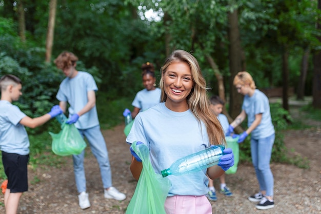 Foto retrato de uma bela mulher com um pequeno grupo de voluntários no fundo com luvas e sacos de lixo limpando o parque da cidade conceito de preservação ambiental e ecologia todos vestindo camisas azuis