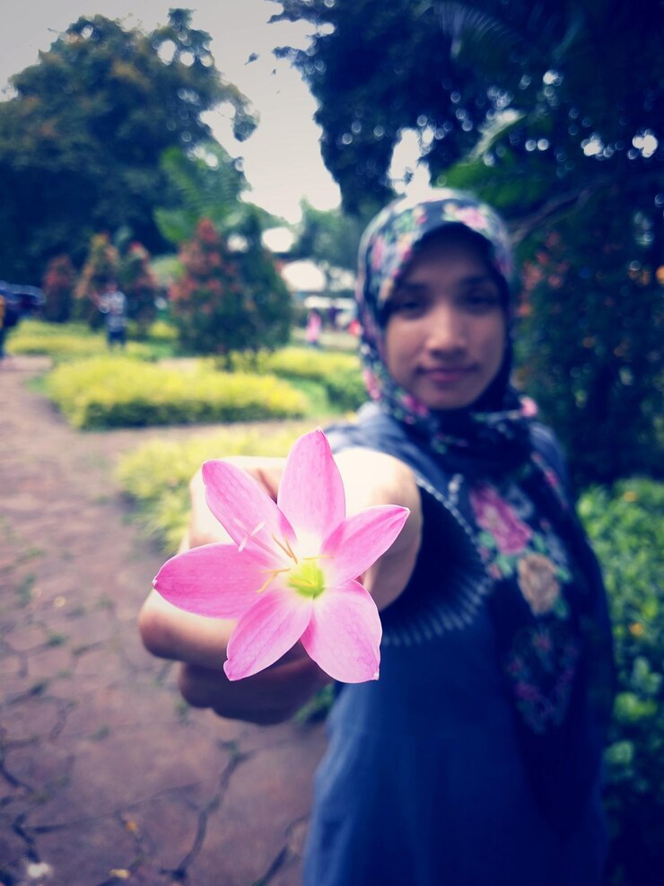 Foto retrato de uma bela mulher de pé junto a uma planta de flores rosa