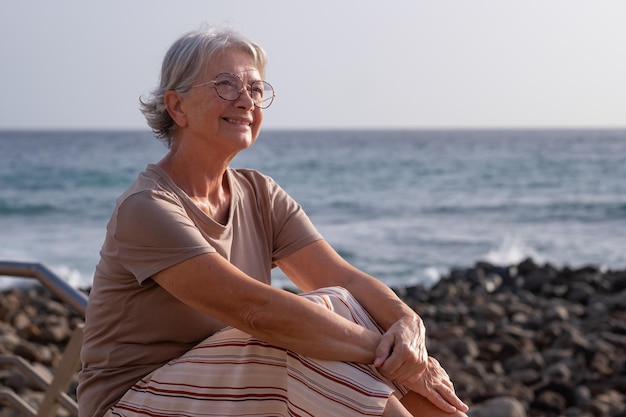 Retrato de uma bela mulher idosa sentada na praia ao pôr do sol olhando para longe sorrindo uma senhora relaxada e idosa gosta de férias e liberdade