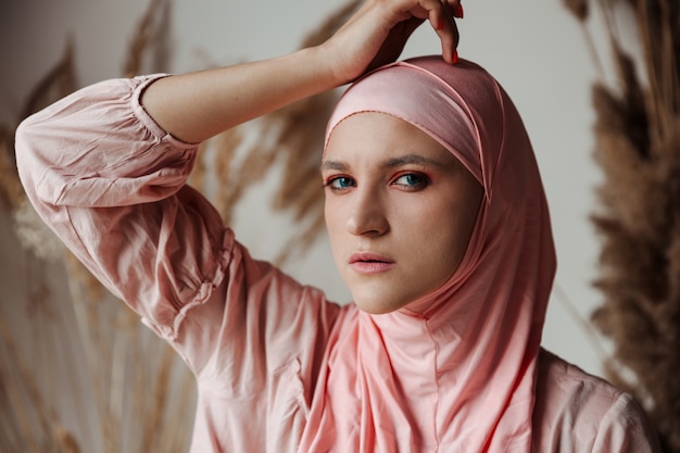 Retrato de uma bela mulher muçulmana árabe usando um hijab rosa, olhando para a câmera