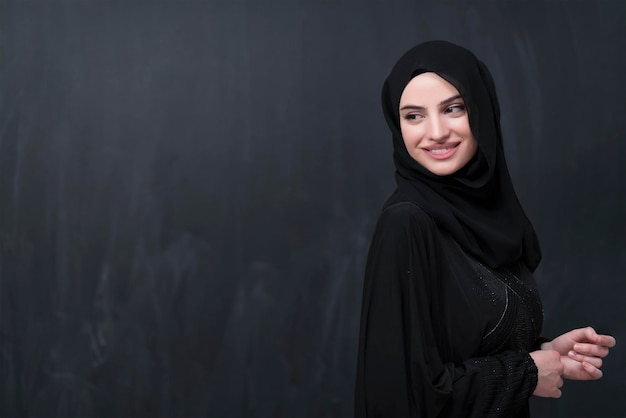 Retrato de uma bela mulher muçulmana em um vestido elegante com hijab na frente do quadro negro, representando a moda moderna do Islã e o conceito de Ramadan Kareem.