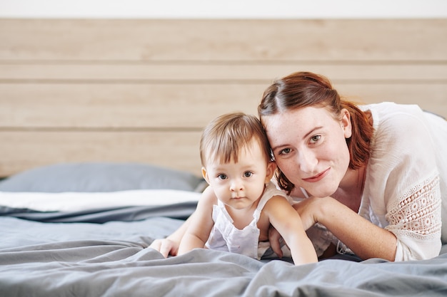 Retrato de uma bela mulher ruiva deitada na cama com sua adorável filha