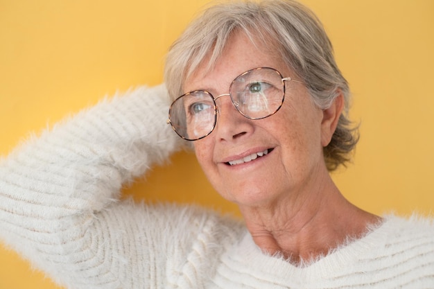 Retrato de uma bela mulher sênior pensativa de cabelos brancos olhando para longe usando óculos isolados em fundo amarelo