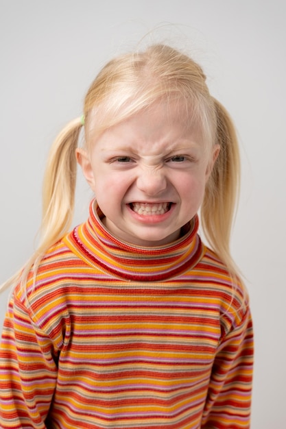 Foto retrato de uma bonita menina sorridente com cabelos loiros em um fundo cinzento