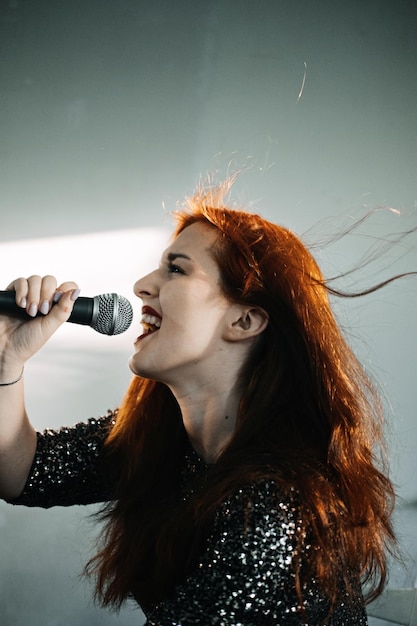 Retrato de uma cantora ruiva em um vestido de noite brilhante segurando o microfone na noite escura