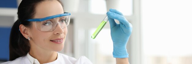 Retrato de uma cientista sorridente com óculos segurando um tubo de ensaio químico em laboratório