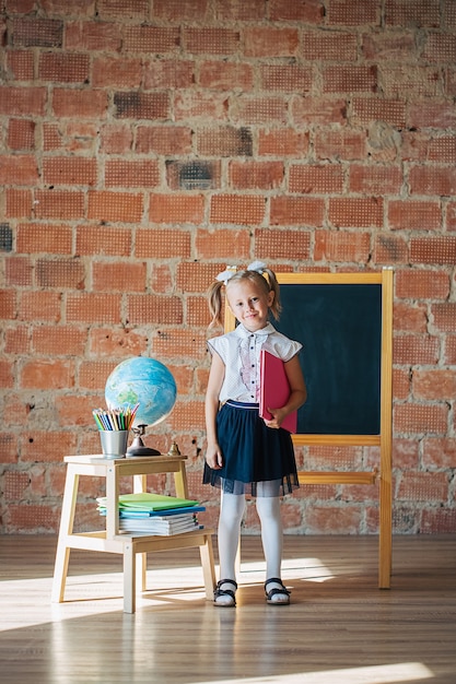 Retrato de uma colegial caucasiana em frente ao quadro-negro com um livro nas mãos, de volta ao conceito de escola