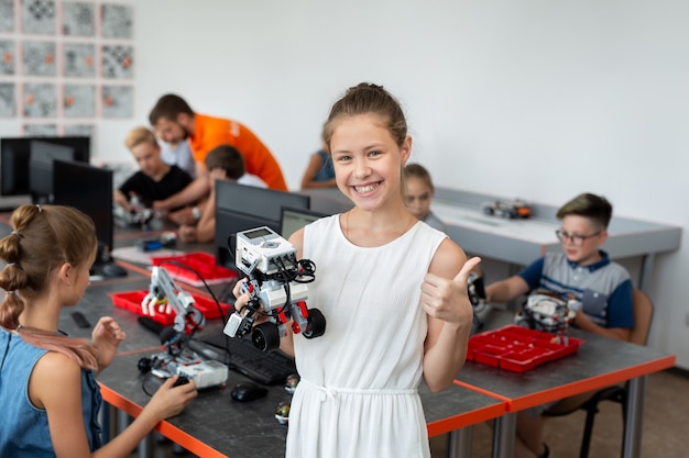 Retrato de uma colegial feliz em uma aula de robótica, ela segura um robô montado com peças de plástico programadas em um computador