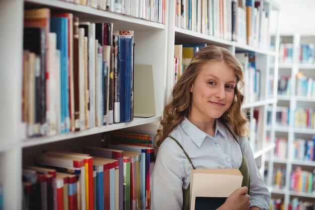 Retrato de uma colegial feliz segurando um livro na biblioteca
