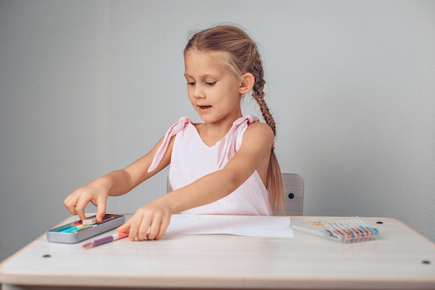 Retrato de uma criança bonita fofo linda sentada em uma mesa branca e levando o lápis nas mãos para desenhar no papel. Conceito de estudo. foto com ruído. foto com ruído