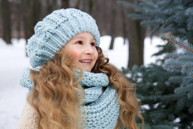 Retrato de uma criança bonitinha linda garota de chapéu e cachecol no dia frio de inverno nevado caminhar no parque e sorrir