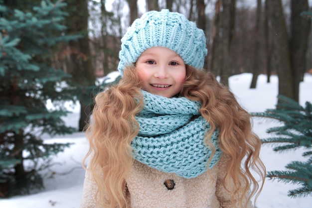 Retrato de uma criança bonitinha linda garota de chapéu e cachecol no dia frio de inverno nevado caminhar no parque e sorrir