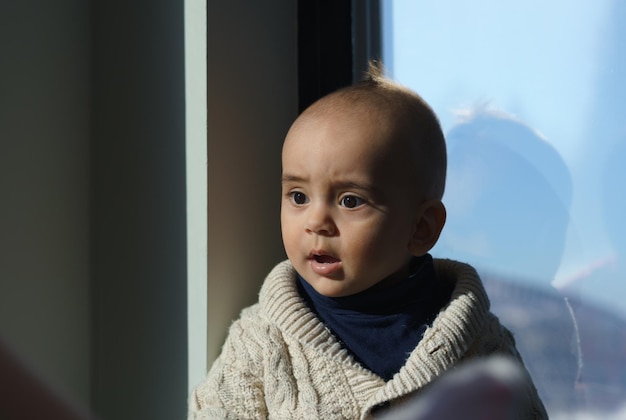 Foto retrato de uma criança com rosto chocado sentado ao lado da janela