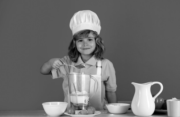 Retrato de uma criança de anos de idade em boné de cozinheiro e avental fazendo salada de frutas e cozinhando comida na cozinha