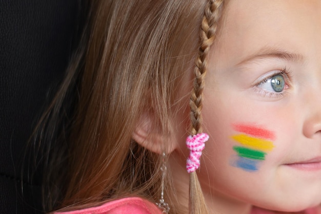 Retrato de uma criança de uma família LGBT com uma bandeira de arco-íris pintada na bochecha para o Dia do Orgulho