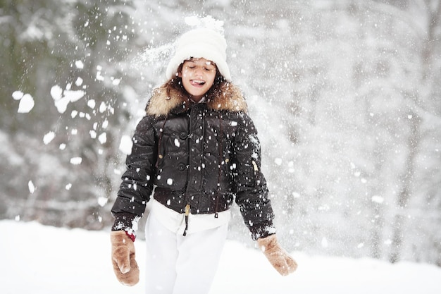 Retrato de uma criança feliz jogando bolas de neve, uma menina de roupas quentes se divertindo com a neve na floresta de inverno