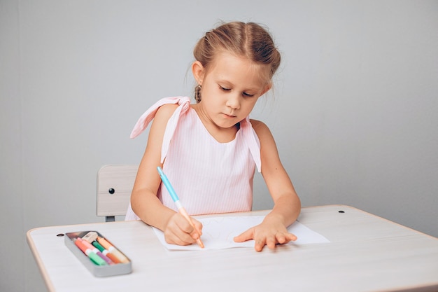 Retrato de uma criança linda linda talentosa, sentado à mesa e desenhando no papel com giz de cera. Conceito de desenho. foto com ruído