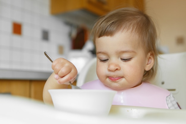 Retrato de uma criança que come comida para bebê com sua colher.