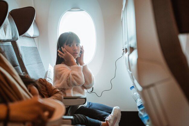 Foto retrato de uma criança sentada em um avião e vendo um filme da tela no assento da frente