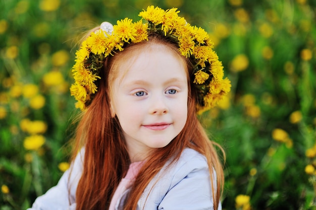 Retrato de uma criança - uma menina ruiva bonita na superfície de um campo de dentes de leão e hortaliças.