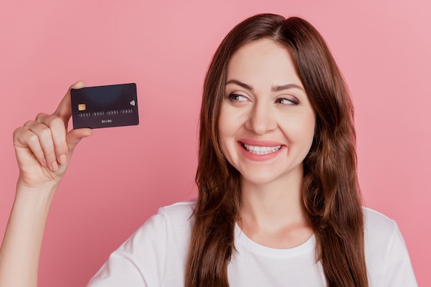 Retrato de uma curiosa consultora de sonho mostrando um sorriso radiante de cartão de crédito, olhar para o lado no fundo rosa