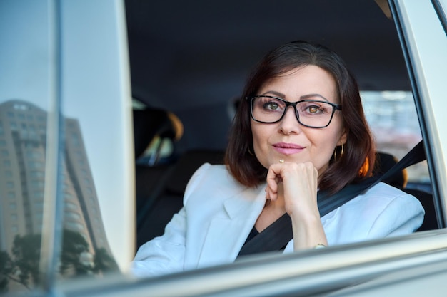 Retrato de uma elegante mulher de meia-idade no carro no banco traseiro do passageiro