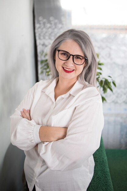 Retrato de uma empresária adulta com cabelos grisalhos em uma posição gerencial, vestida com uma blusa branca e ocupada trabalhando no escritório