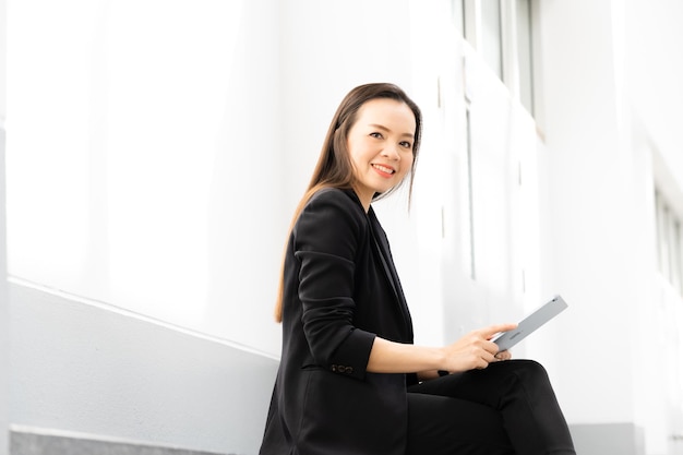 Retrato de uma empresária asiática de meia-idade segurando um tablet e sorrindo para a câmera