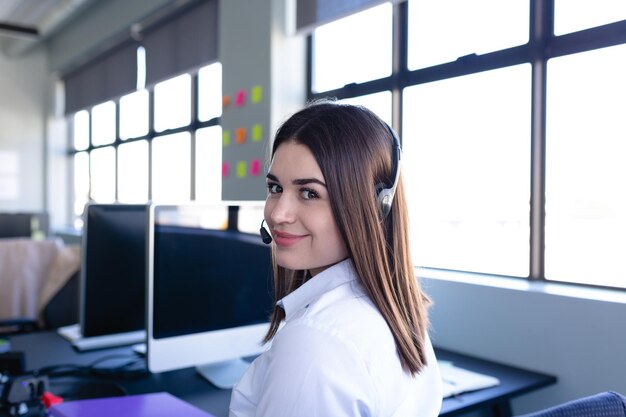 Foto retrato de uma empresária caucasiana vestindo roupas elegantes e fones de ouvido, trabalhando em um escritório moderno, sentada perto de uma mesa e olhando diretamente para uma câmera. distanciamento social e auto-isolamento