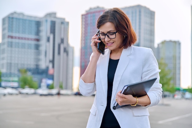 Retrato de uma empresária madura bem-sucedida com smartphone ao ar livre