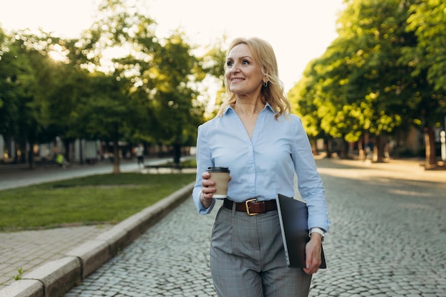 Retrato de uma empresária madura bem-sucedida vestindo roupas elegantes Mulher de 50 anos Mulher segurando laptop e xícara de café enquanto caminhava na cidade Estilo de vida e conceito de trabalho