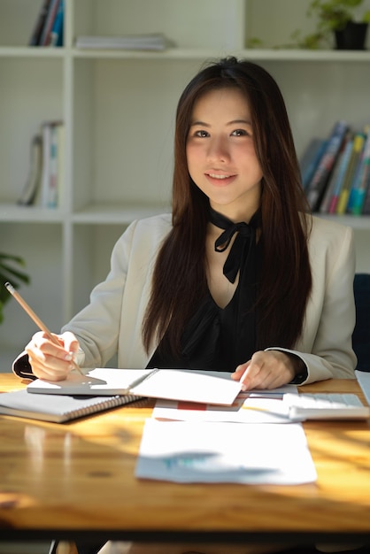 Retrato de uma encantadora empresária asiática ou secretária feminina sentada em sua mesa de escritório