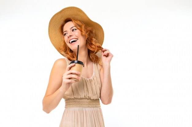 retrato de uma encantadora menina sorridente com um chapéu com um copo de papel de chá na parede branca