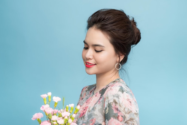 Retrato de uma encantadora mulher asiática com buquê de flores sobre fundo azul