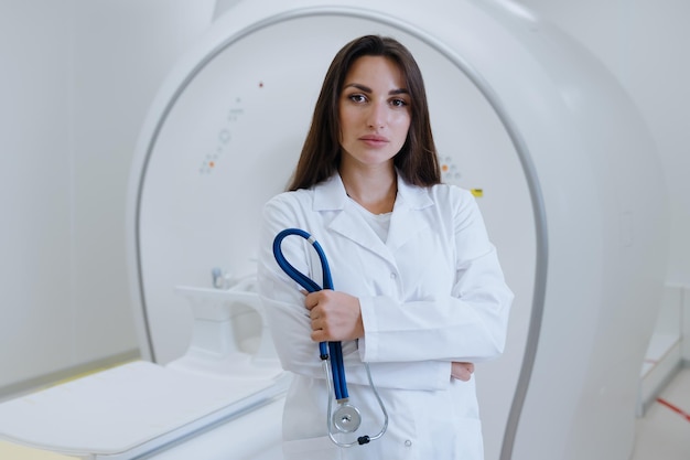 Retrato de uma enfermeira de jaleco branco segurando um estetoscópio no fundo de um scanner de tomografia computadorizada na clínica
