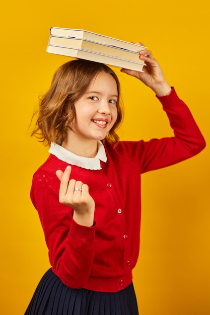 Retrato de uma estudante adolescente feliz de uniforme segurando livros na cabeça