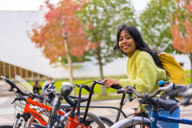 Retrato de uma estudante asiática sorridente estacionando uma bicicleta no campus da faculdade