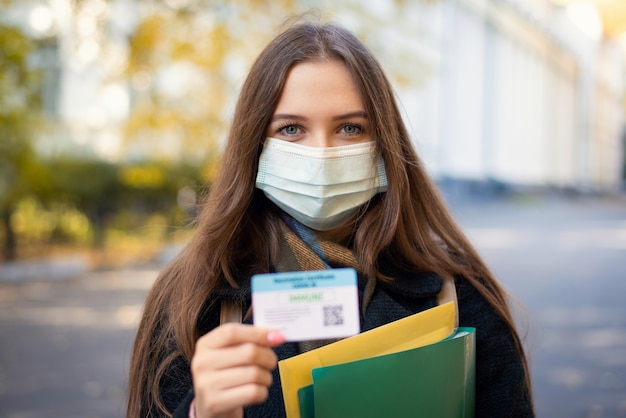 Retrato de uma estudante com certificado de vacinação em pé perto do prédio da universidade