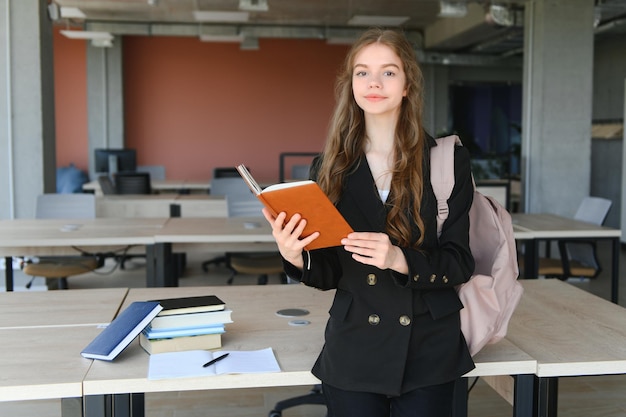 Retrato de uma estudante em pé na sala de aula com um livro nas mãos