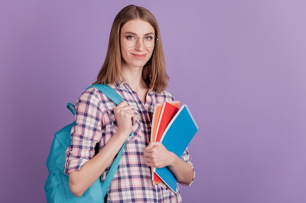 Retrato de uma estudante jovem e atraente segurando um caderno em sua bolsa de mãos, educação isolada em um fundo de cor violeta.