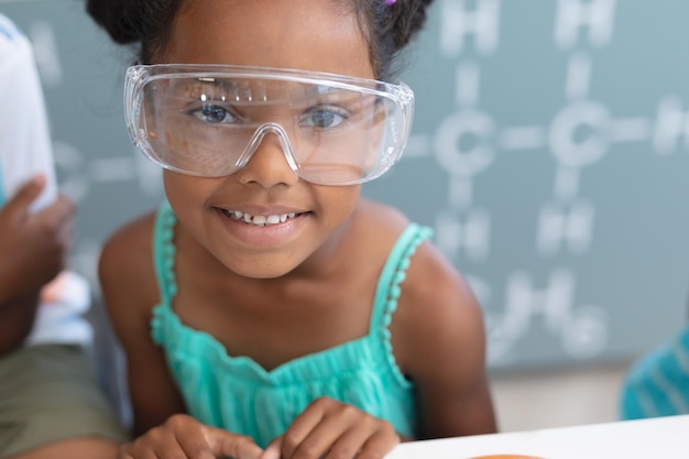 Retrato de uma estudante primária afro-americana sorridente usando óculos de proteção em laboratório